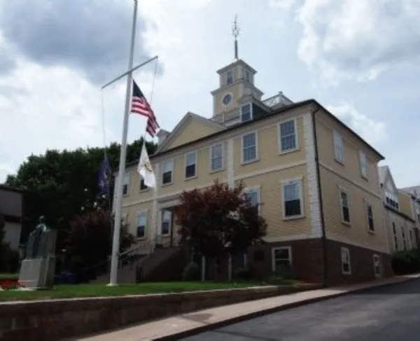 A historic yellow civic building stands behind a flagpole flying the American flag.