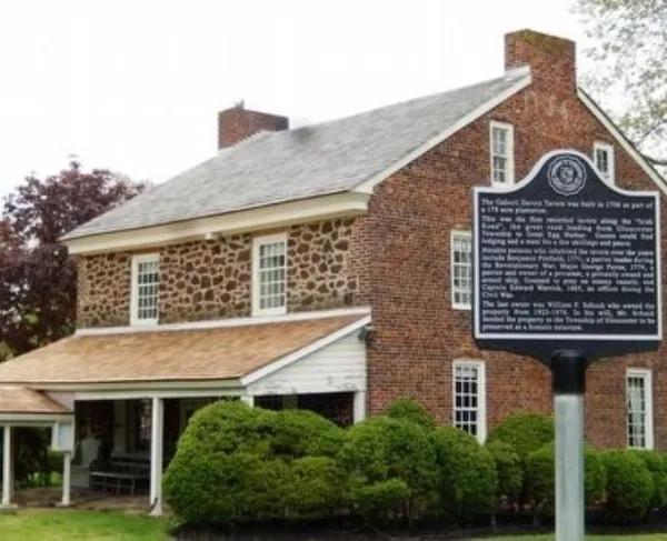 A historic stone-and-brick tavern with white trim stands behind a black marker describing its 1756 origins.