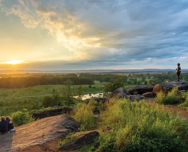 A couple sits on the rocks at Little Round Top at sunset