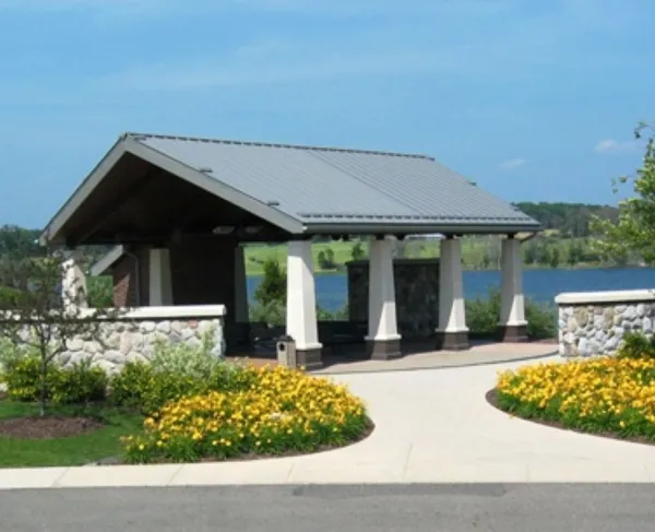 A covered shelter surrounded by yellow flowers and a rock wall. In the background is a body of water,