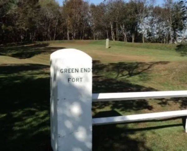 A white stone marker labeled “Green End Fort” stands in a grassy landscape with bare trees and a bright blue sky.
