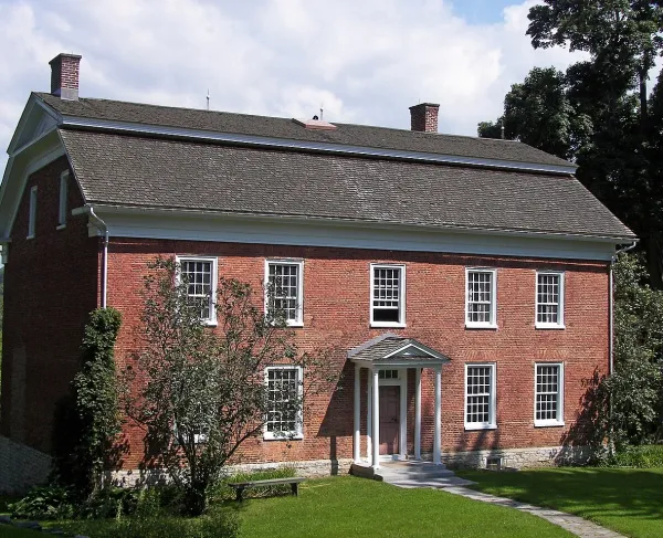 Red brick 2-story colonial home with a gambrel roof, two chimneys, and 9 windows trimmed in white.and 