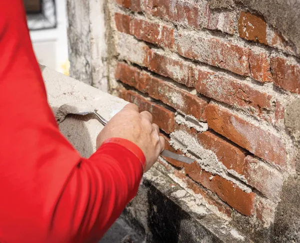 An individual's arm is seen applying mortar to a brick wall.