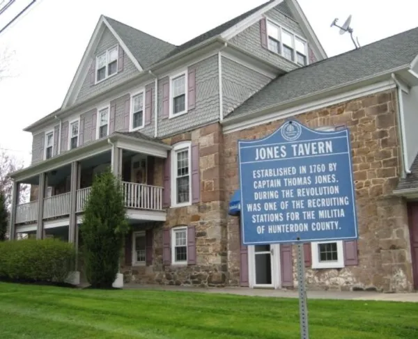 A stone‑and‑shingle historic building with a columned porch stands behind a blue marker identifying it as Jones Tavern, established in 1760.