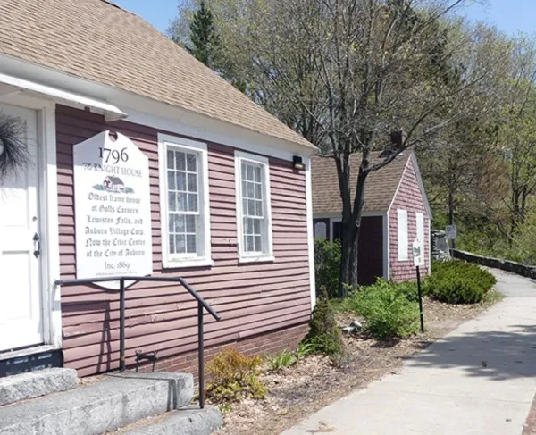 Historic red clapboard Knight House (1796) with a white entrance sign, situated along a sidewalk lined with trees.