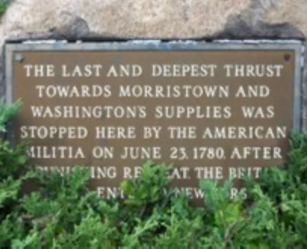 A bronze plaque mounted on a stone surrounded by greenery commemorates a June 23, 1780 militia action that halted a British advance toward Morristown.