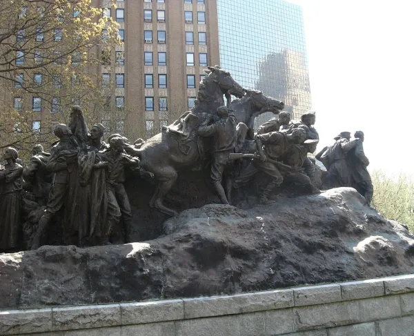 A large bronze monument shows soldiers and civilians in dramatic motion, with horses and figures emerging from a rugged base in an outdoor urban park.