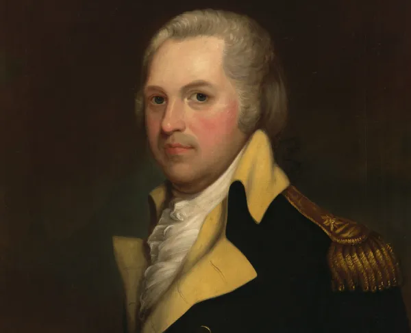 A man with white hair sits and looks at the viewer wearing the blue coat of the Continental Army with buff-colored lapels and a gold epaulet. A ruffled shirt peaks out from under his coat. 