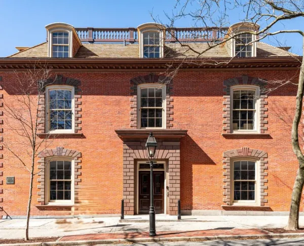 A three‑story brick brownstone building with symmetrical windows and a central stone‑framed entrance stands behind a black streetlamp.