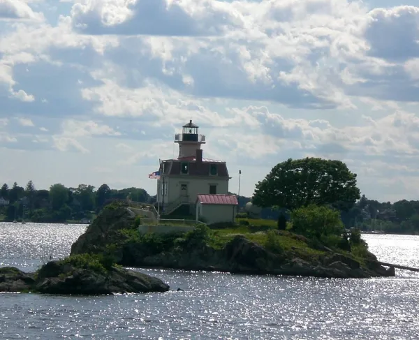 A small rocky island with a cream-colored lighthouse and red roof surrounded by water.