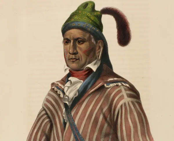 A Native American man wear a green cap and a red and white striped shirt. 