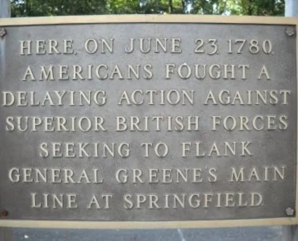 A bronze plaque mounted on a stone surface commemorates a June 23, 1780 battle where Americans delayed advancing British forces near Springfield.