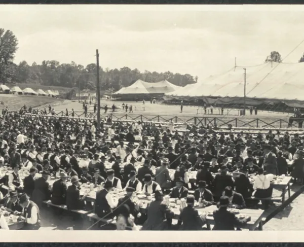 Black and white photograph of an outdoor mess hall with rows of men seated at long tables
