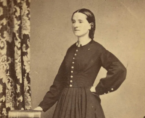 Full-length studio portrait of Civil War surgeon Mary Edwards Walker standing in profile with one hand resting on a book.