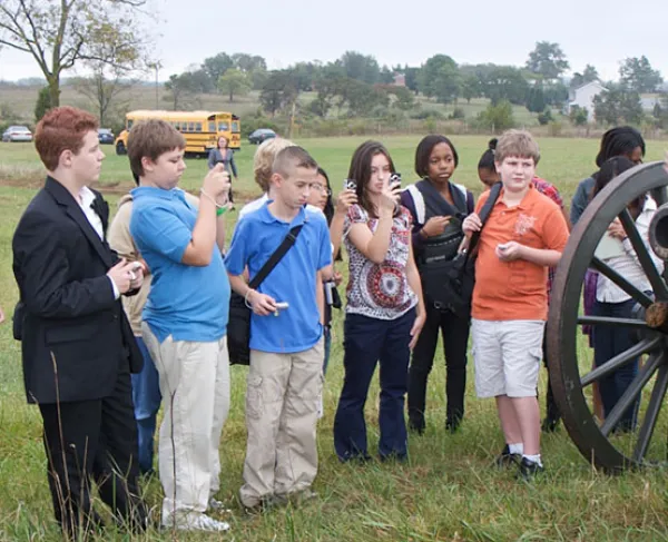 This image depicts a tour guide presenting to a group in front of a battlefield cannon.