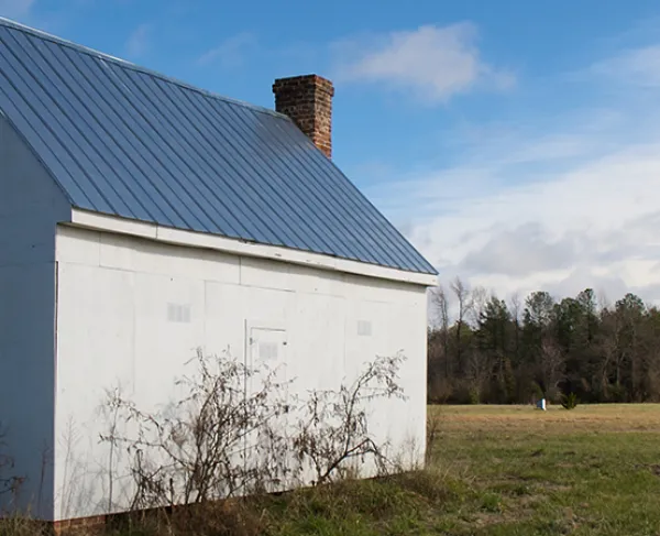 Photograph of a white brick building in the foreground with a battlefield in the background. 