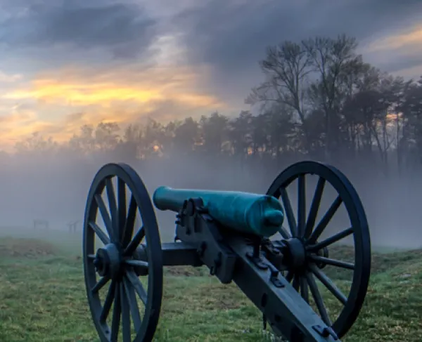Cannons in a line at Chancellorsville Battlefield on a foggy morning as day breaks.