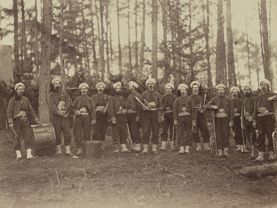 Sepia toned photo of a group of soldiers in the woods in uniform with their band instruments