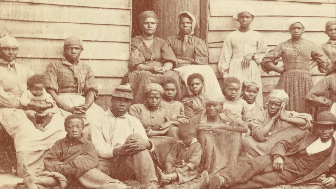 Group of African American men, women, and children seated and standing outside a wooden building at Cumberland Landing, Virginia, in 1862.
