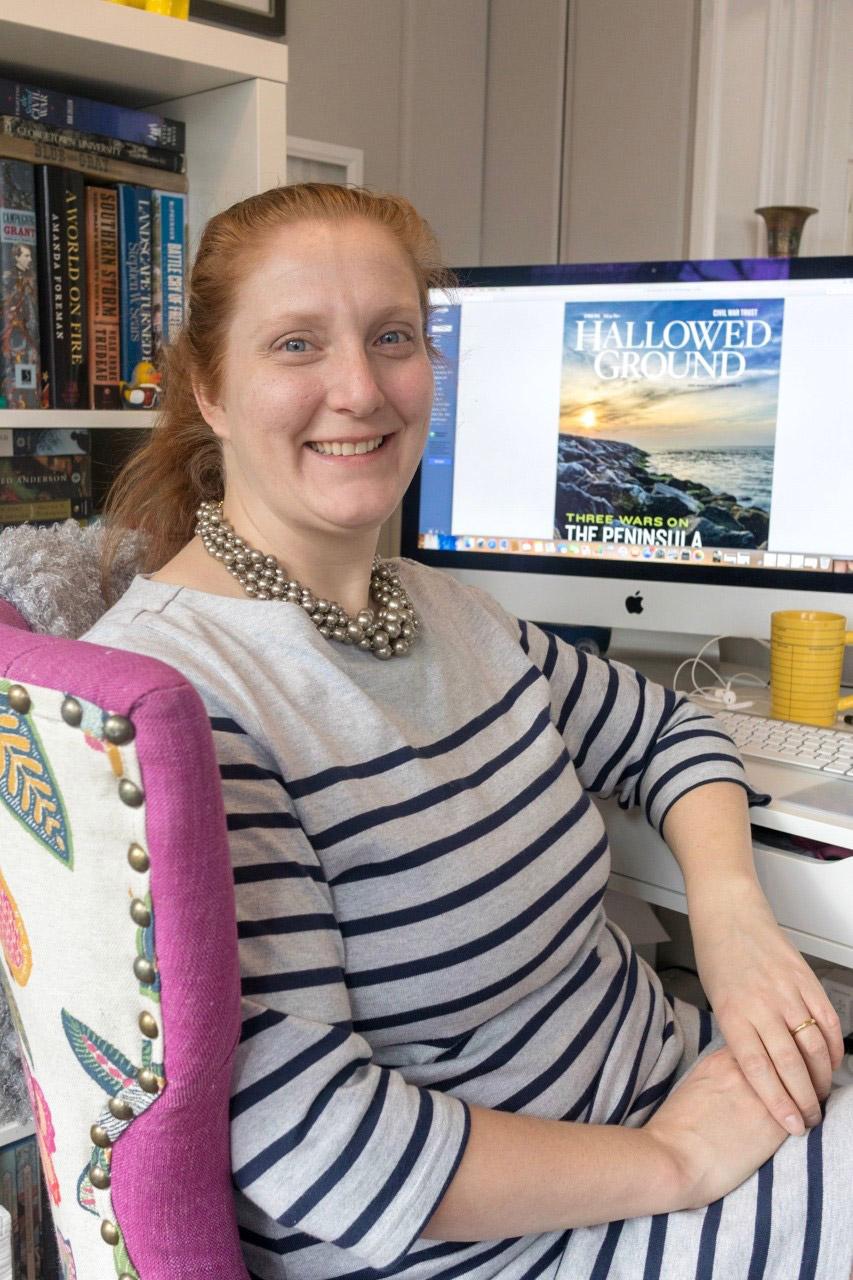 Portrait of Mary Koik with the cover of an issue Hallowed Ground on her monitor screen