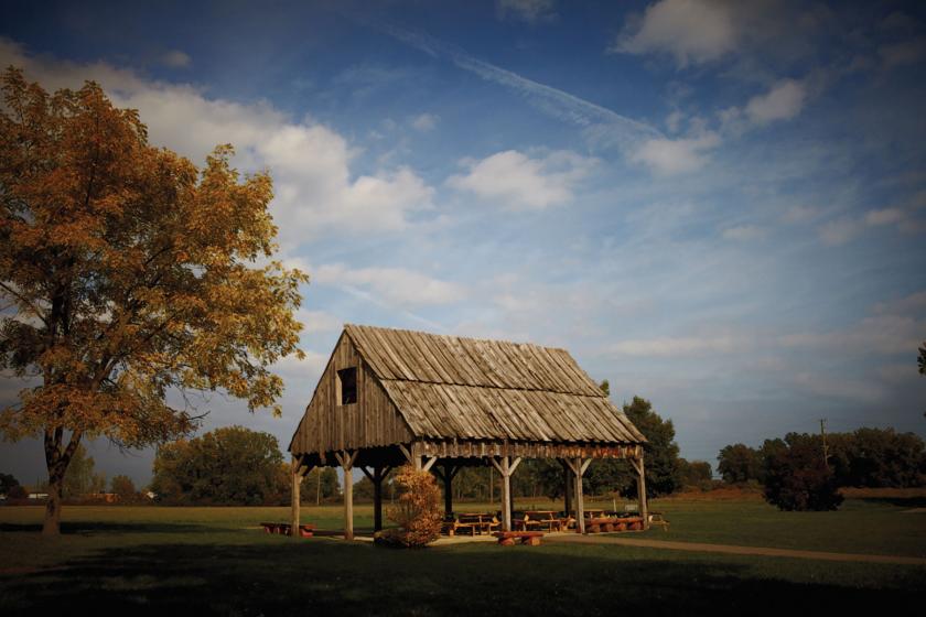 Wooden. shelter with picnic table and benches beneath it at a park setting