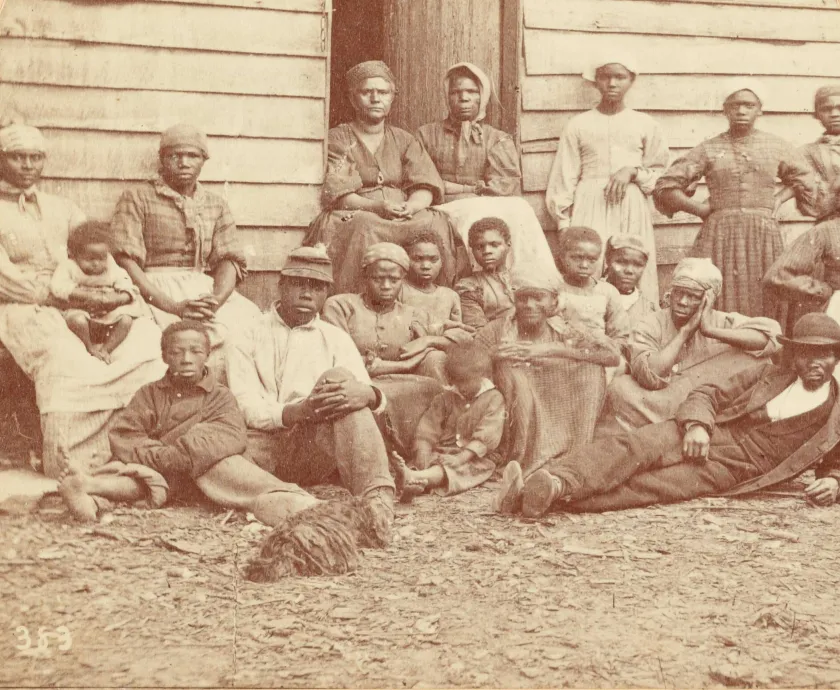 Group of African American men, women, and children seated and standing outside a wooden building at Cumberland Landing, Virginia, in 1862.