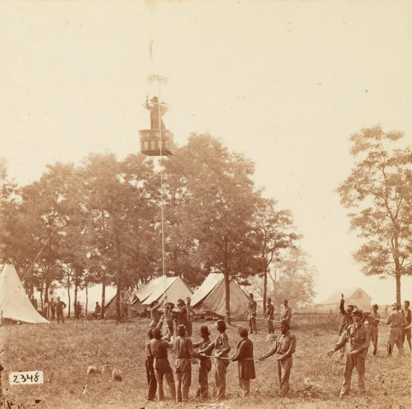 Union Army aeronaut Thaddeus S. C. Lowe observes the Battle of Fair Oaks, Virginia, from his observation balloon Intrepid, while soldiers below hold its tethering ropes.