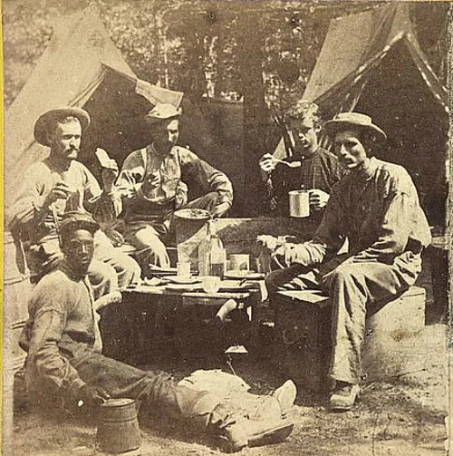 Union soldiers gathered around a table for a meal in camp.