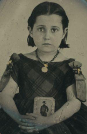 A young girl in mourning dress with a portrait of her father on her lap.