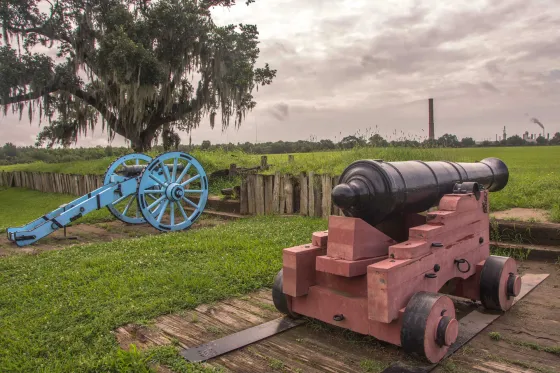 Two cannons stand upon Chalmette Battlefield, La. surrounded by urbanization.