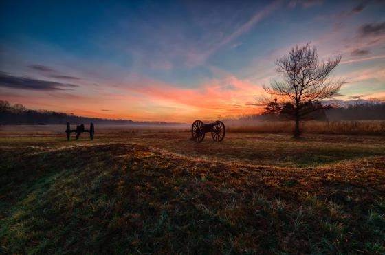 Sunset at Chancellorsville Battlefield. Two cannons and a bare tree stand in the foreground.