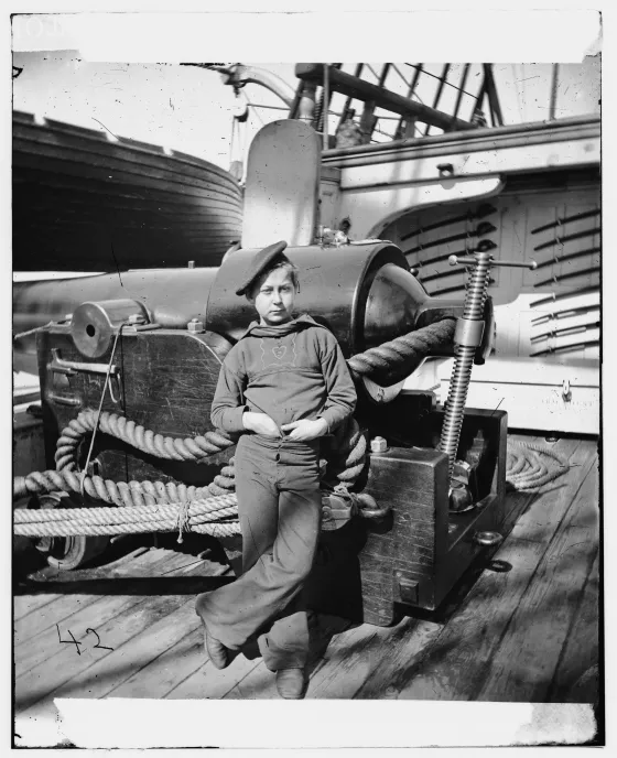 Civil War-era photograph of a young sailor standing beside a large naval gun aboard the USS New Hampshire off Charleston, South Carolina.