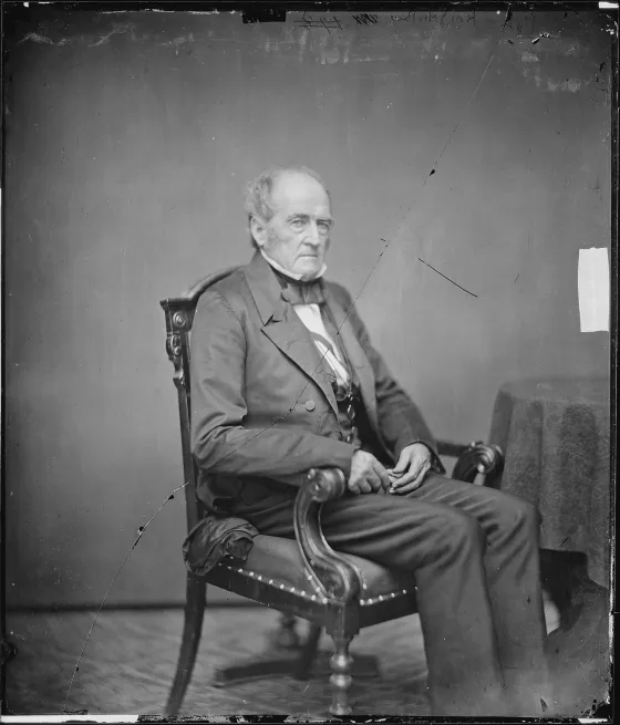 Portrait photograph of John Bell seated in a chair, wearing a dark suit and bow tie.