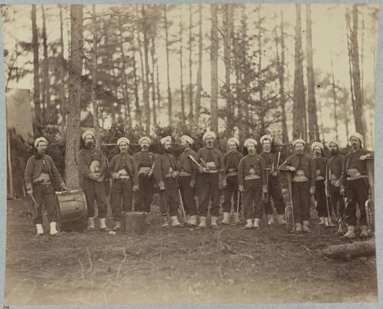 Sepia toned photo of a group of soldiers in the woods in uniform with their band instruments