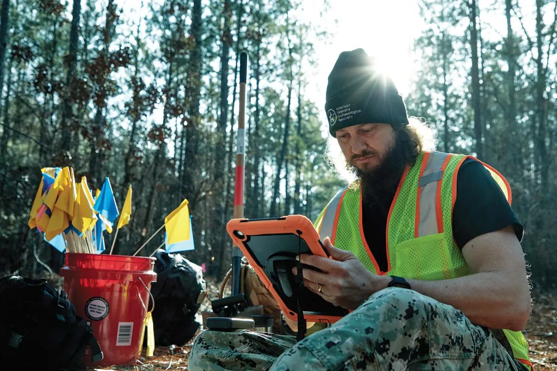 A veteran in a bright yellow vest logs an artifact with a GPS tracking program.
