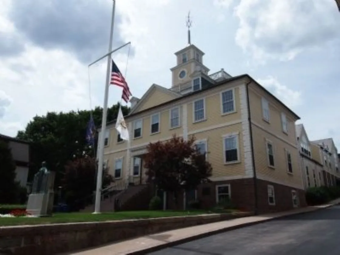A historic yellow civic building stands behind a flagpole flying the American flag.