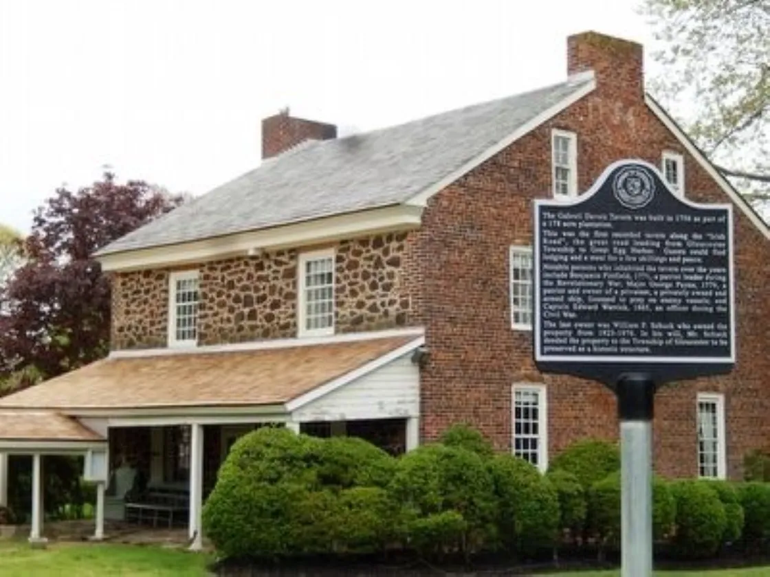 A historic stone-and-brick tavern with white trim stands behind a black marker describing its 1756 origins.