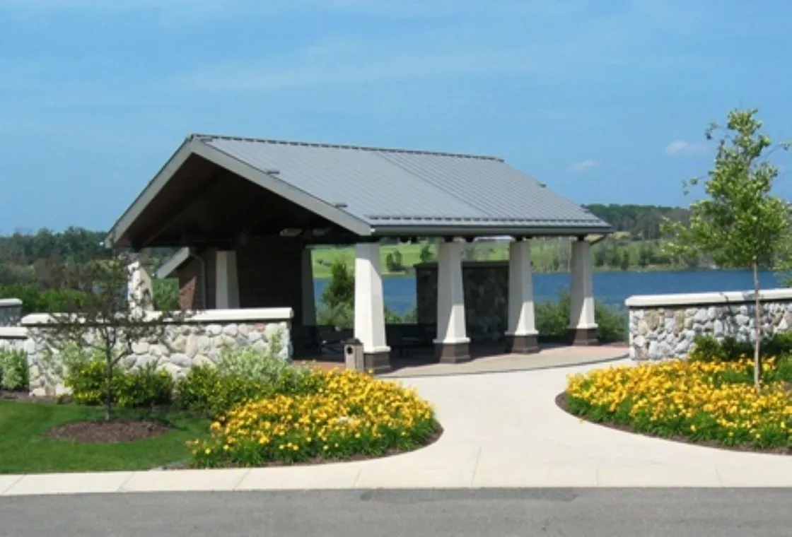 A covered shelter surrounded by yellow flowers and a rock wall. In the background is a body of water,