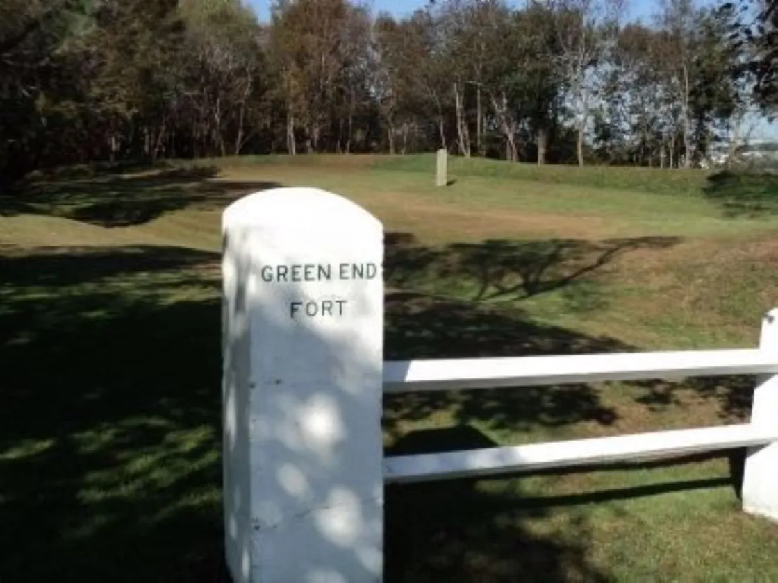 A white stone marker labeled “Green End Fort” stands in a grassy landscape with bare trees and a bright blue sky.