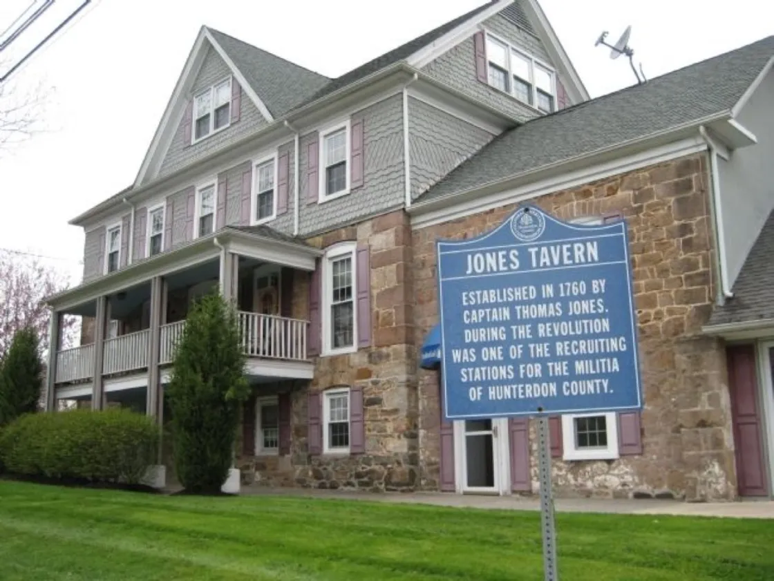 A stone‑and‑shingle historic building with a columned porch stands behind a blue marker identifying it as Jones Tavern, established in 1760.