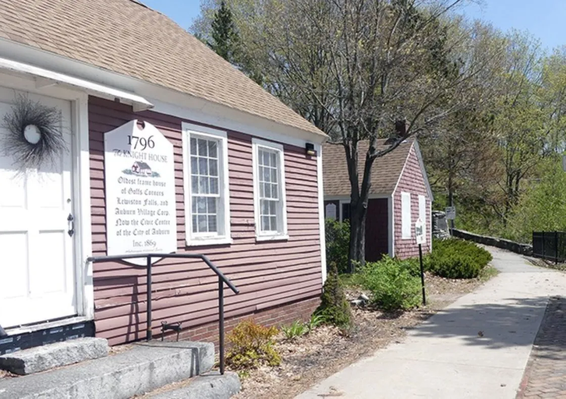 Historic red clapboard Knight House (1796) with a white entrance sign, situated along a sidewalk lined with trees.