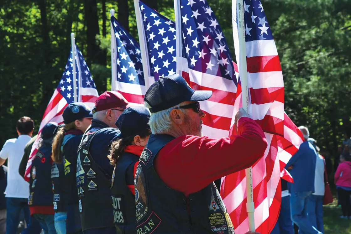 Veterans stand with American flags during the solemn reinterment ceremony at Lake George Battlefield Park, where the remains of 44 individuals were laid to rest.