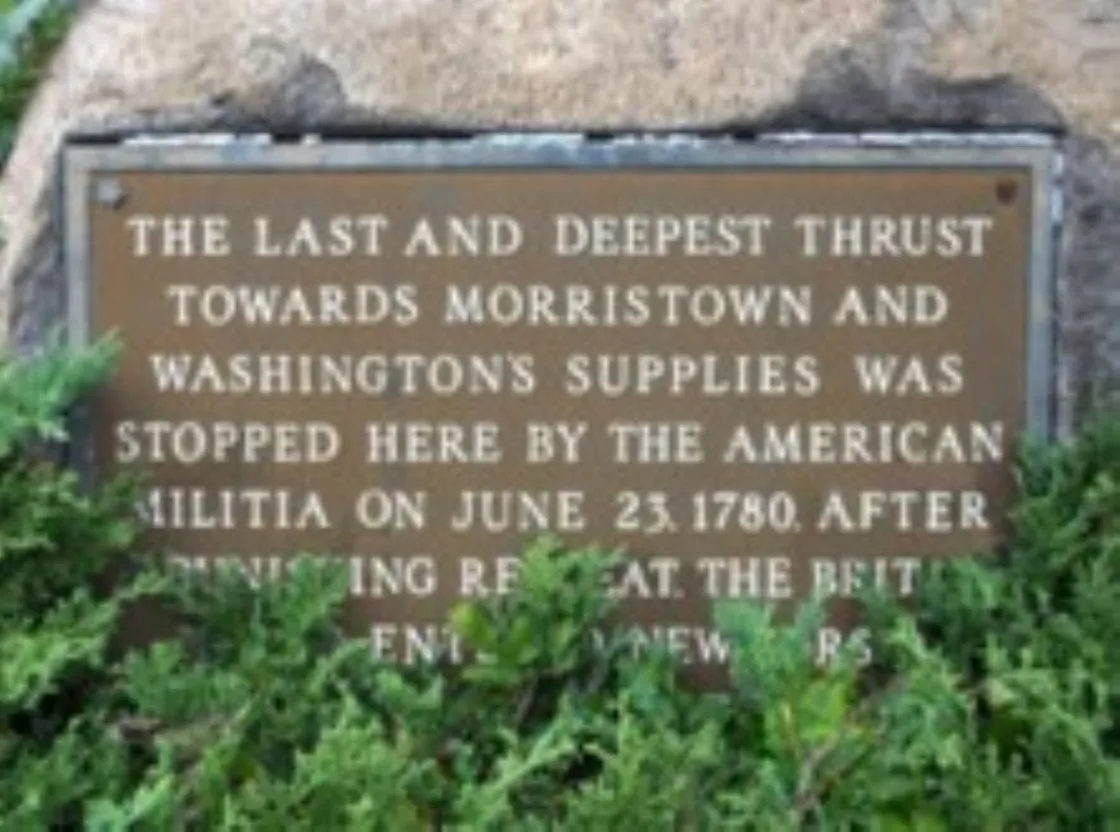A bronze plaque mounted on a stone surrounded by greenery commemorates a June 23, 1780 militia action that halted a British advance toward Morristown.