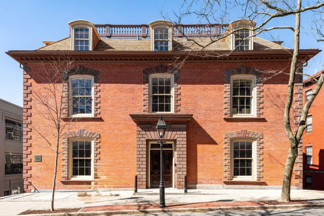 A three‑story brick brownstone building with symmetrical windows and a central stone‑framed entrance stands behind a black streetlamp.