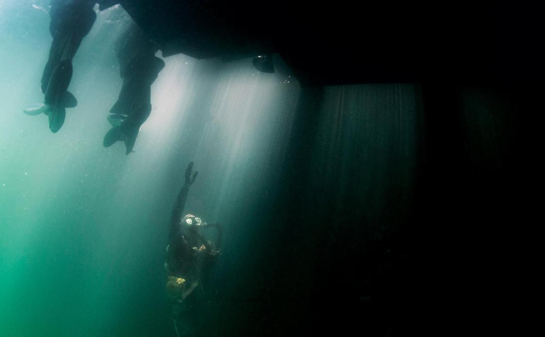 Underwater photo showing a diver reaching up towards the underpart of a boat