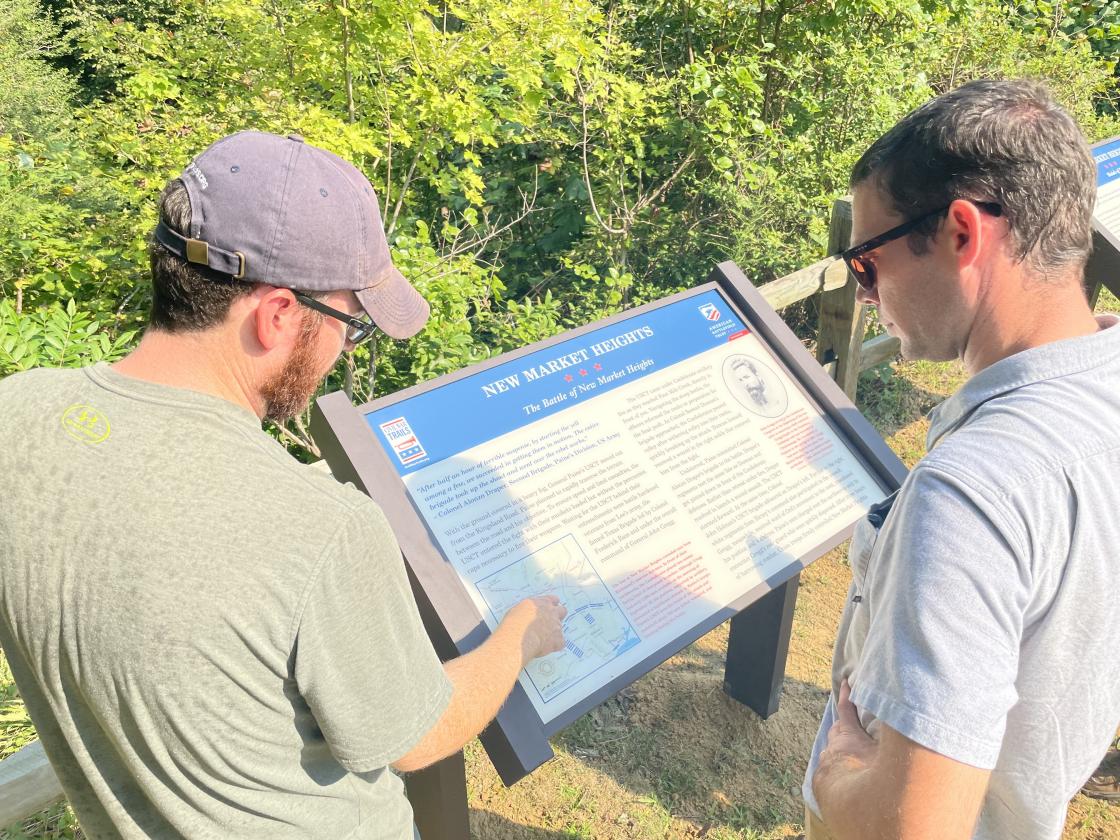 Two men read descriptive signage on a battlefield