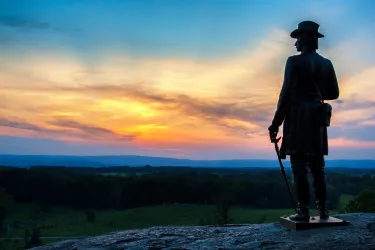 A statue stands at Little Round Top against a vibrant sunset.