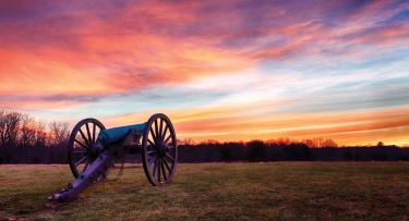 A cannon at Manassas National Battlefield Park under a vivid orange-purple sky.