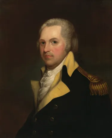A man with white hair sits and looks at the viewer wearing the blue coat of the Continental Army with buff-colored lapels and a gold epaulet. A ruffled shirt peaks out from under his coat. 