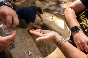 A hand holding a flattened musket ball at the dig site.